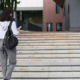 900-a-female-student-with-a-black-backpack-and-a-notebook-in-her-hands-stands-on-the-steps-in-front-of-the-institute-higher-education-the-beginning-of-the-school-year-back-to-school-copyspace